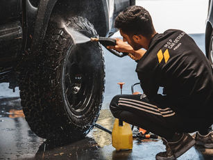 A Temecula Auto Wraps detailer in a branded MDP jacket cleaning a wheel